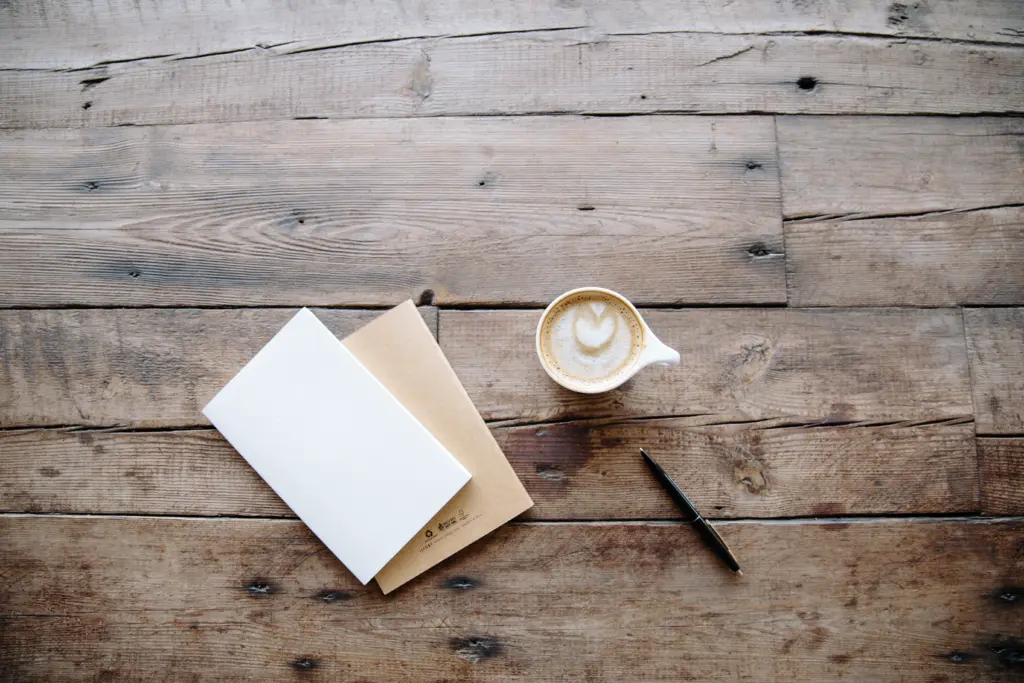 Cup of coffee next to notebooks and a pen on a wooden desk
